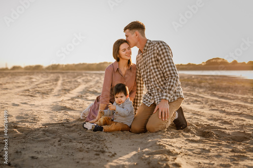 One year old boy with mom and dad sitting on the river bank and playing with sand