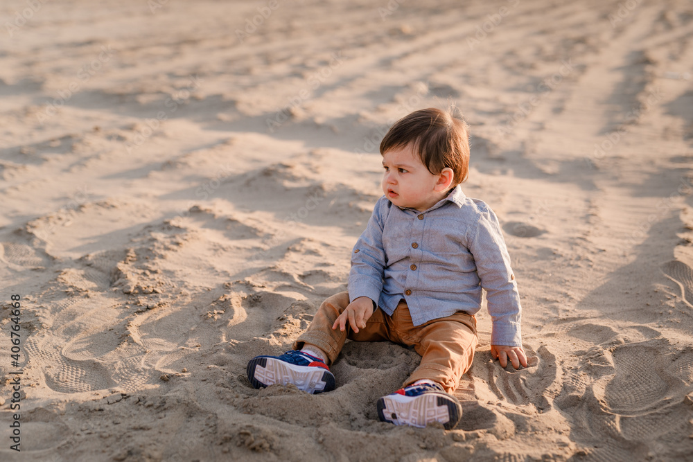 One-year-old boy sitting in the sand, smiling and playing One-year-old boy sitting in the sand, smiling and playing
