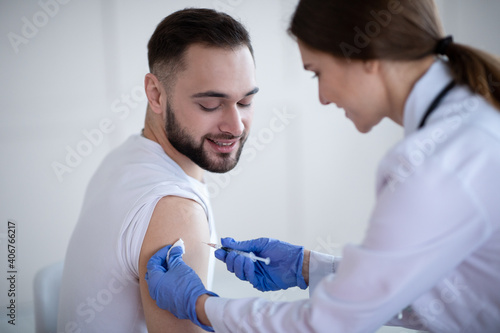 Female medic giving male patient shot of coronavirus vaccine at clinic. Healthcare and medical service concept