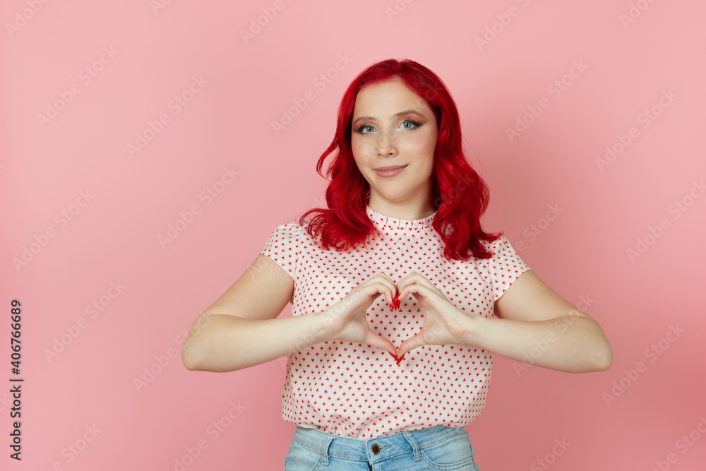 close-up a beautiful woman with red hair makes a heart sign from the fingers of her hands in front of her , isolated on a pink background. close-up a beautiful woman with red hair makes a heart sign from the fingers of her hands in front of her , isolated on a pink background.