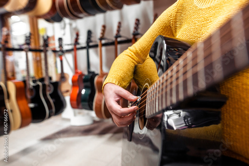 Young woman trying and buying a new wooden guitar in instrumental or musical shop, instrument concept