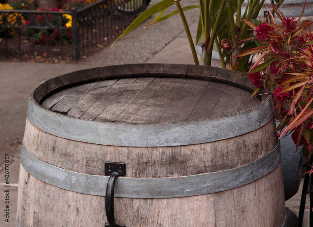 a rustic wooden barrel head standing on its side like a table on a sidewalk surrounded by plants, with metal bands showing, space to place objects or copy