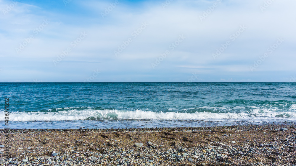 Blue sea with waves, pebble beach and cloudy sky Blue sea with waves, pebble beach and cloudy sky