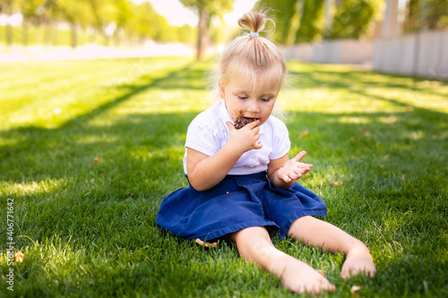 little blonde girl in school uniform sitting or lying on the grass eating delicious sweet cookies