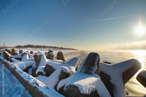 Curonian spit pier with protecting barrier rocks, dunes and an empty beach covered by snow. Beautiful sunny weather and blue sky. Klaipeda Lithuania