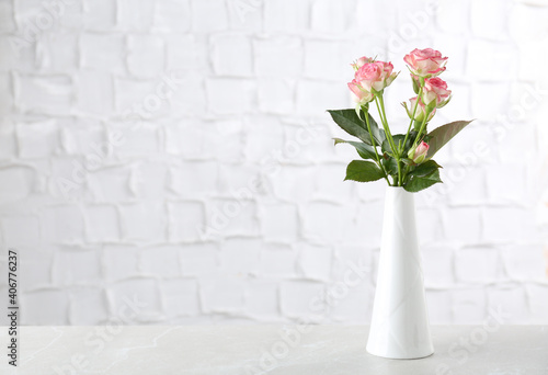 Vase with beautiful pink roses on white table near brick wall