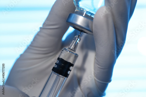 Woman filling syringe with vaccine from vial on blurred background, closeup photo