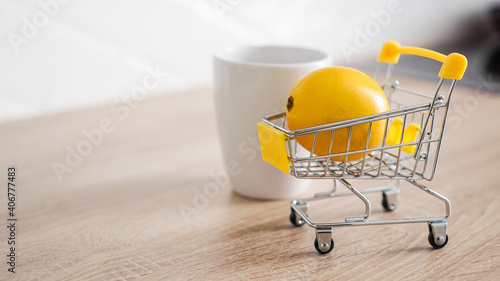 Lemon in a small shopping cart on the kitchen table. Nearby is a white mug of tea. Light and modern kitchen background.