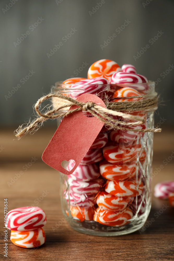 Colorful hard candies in glass jar on wooden table