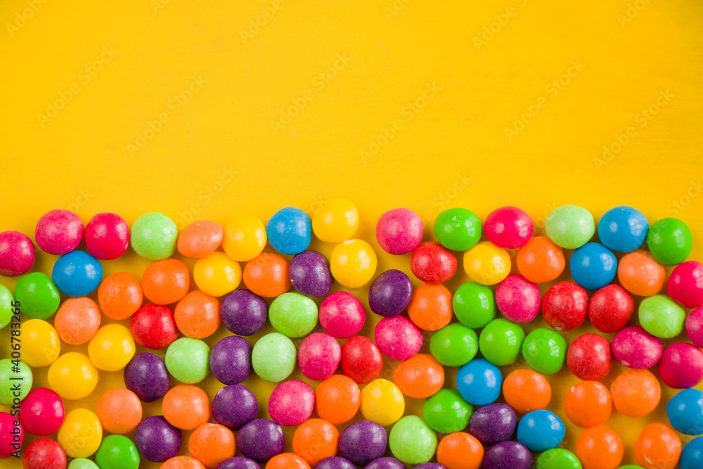 Obraz premium Skittles candy on the yellow table, colorful sweet candy background