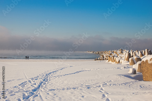 Fototapeta Naklejka Na Ścianę i Meble -  Curonian spit pier with protecting barrier rocks covered by snow. Beautiful sunny weather and blue sky. Klaipeda Lithuania,