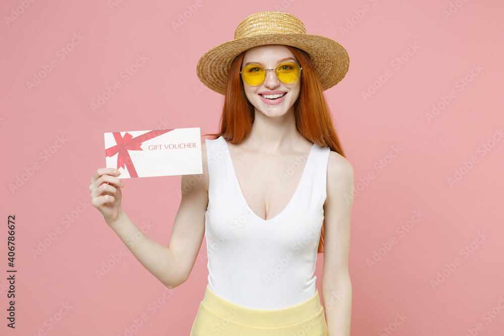 Young smiling nice redhead woman 20s ginger long hair wearing straw hat glasses summer clothes holding gift voucher flyer mock up look camera isolated on pastel pink color background studio portrait. Young smiling nice redhead woman 20s ginger long hair wearing straw hat glasses summer clothes holding gift voucher flyer mock up look camera isolated on pastel pink color background studio portrait.
