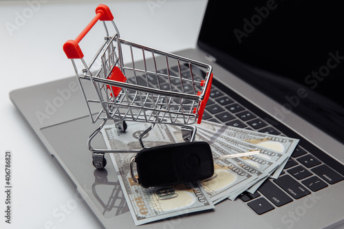 Car keys with dollar banknotes and shopping cart on laptop's keyboard. Online purchase car concept.