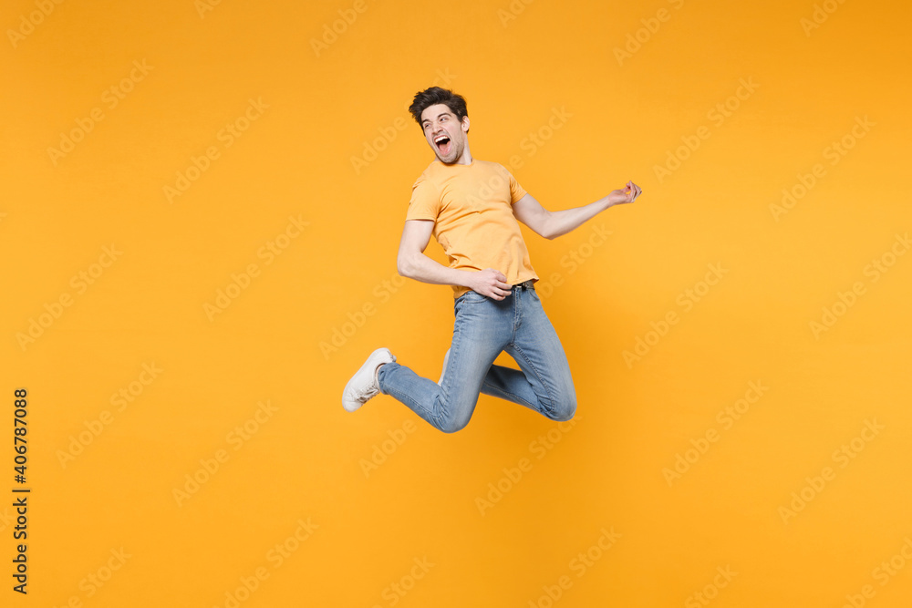 Full length of young caucasian fun happy excited man 20s wearing casual basic t-shirt jeans high jumping up play guitar hand gesture expression isolated on yellow color background studio portrait