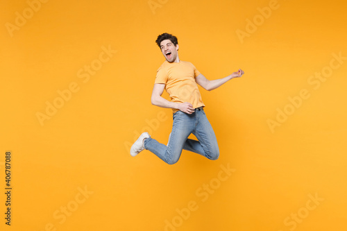 Full length of young caucasian fun happy excited man 20s wearing casual basic t-shirt jeans high jumping up play guitar hand gesture expression isolated on yellow color background studio portrait © ViDi Studio