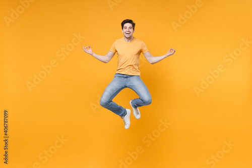 Full length body of young meditating happy excited man 20s in casual t-shirt jeans high jump up levitating hold hands in yoga om gesture look camera isolated on yellow background studio portrait.