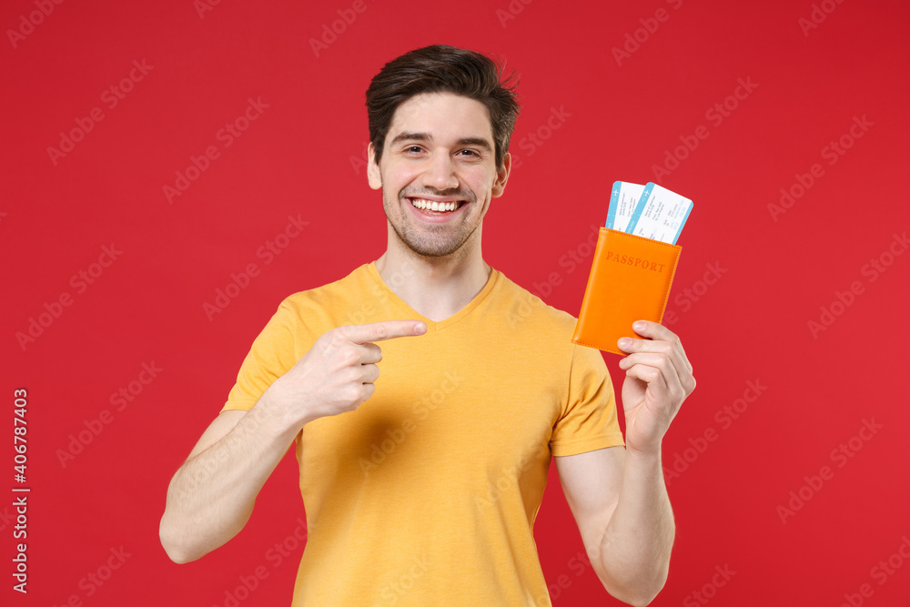 Traveler tourist man wearing yellow casual t-shirt hold pointing finger on passport tickets isolated on red color background. Passenger travel abroad on weekends getaway. Air flight journey concept. Traveler tourist man wearing yellow casual t-shirt hold pointing finger on passport tickets isolated on red color background. Passenger travel abroad on weekends getaway. Air flight journey concept.