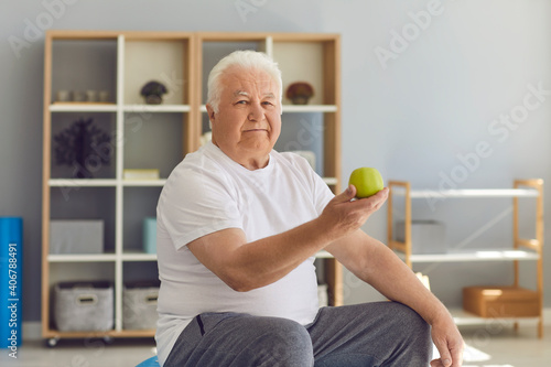 Portrait of an older man sitting in a chair and about to enjoy a green fresh apple.