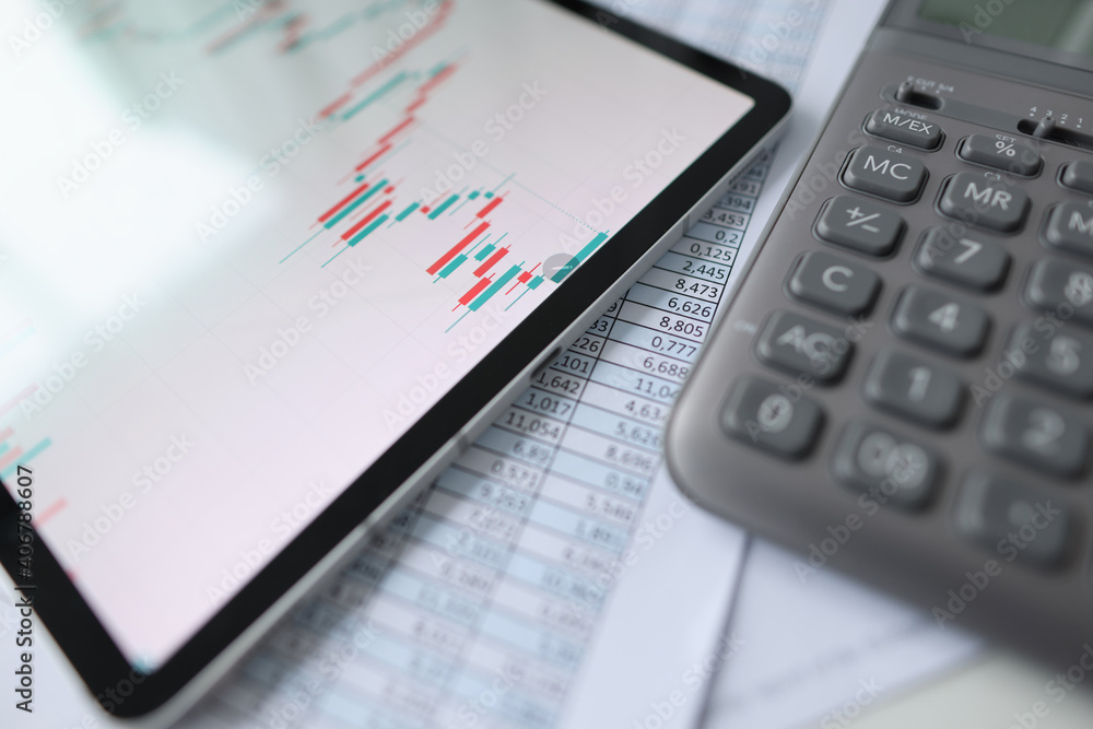 On table is tablet with commercial charts, calculator and documents with reports On table is tablet with commercial charts, calculator and documents with reports