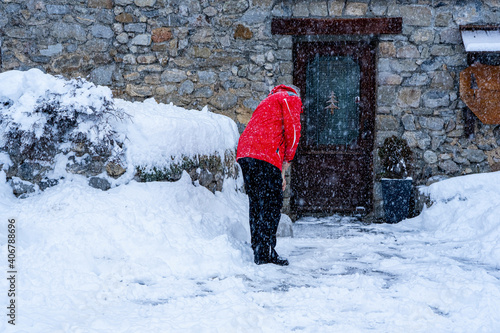 Fototapeta Naklejka Na Ścianę i Meble -  Man with snow shovel cleans sidewalks in winter near house. Winter time, snowfall. France Europe.