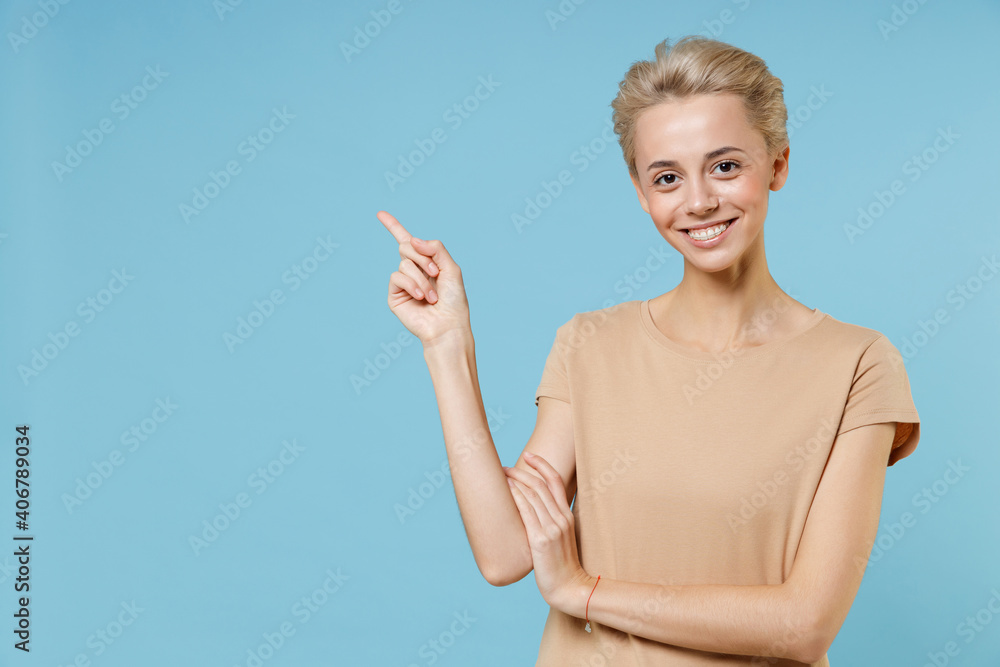 Young smiling blonde woman short haircut dental braces in casual basic beige t-shirt pointing index fingers aside on copy space area workspace look camera isolated on blue background studio portrait. Young smiling blonde woman short haircut dental braces in casual basic beige t-shirt pointing index fingers aside on copy space area workspace look camera isolated on blue background studio portrait.