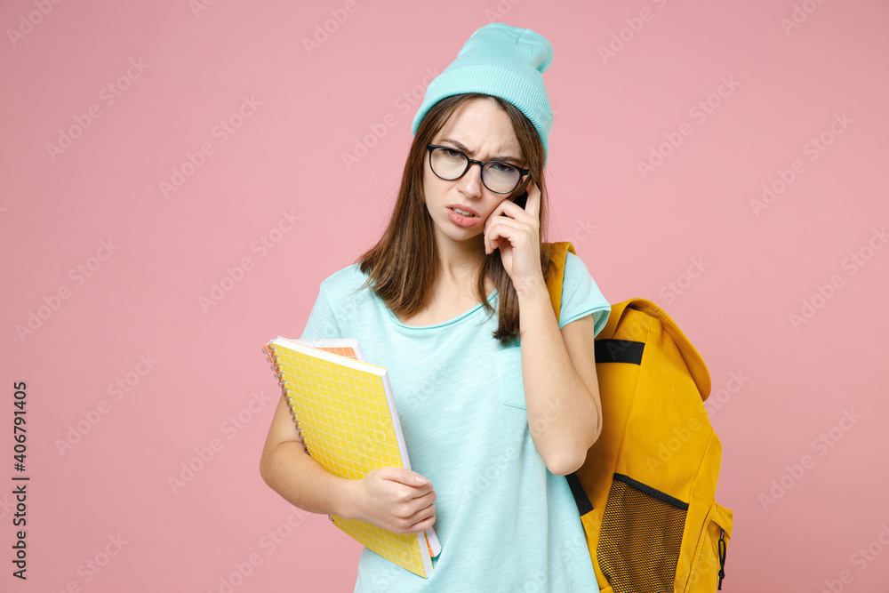 Displeased tired woman student in blue t-shirt hat glasses backpack hold notebooks put hand on head isolated on pink background studio portrait. Education in high school university college concept. Displeased tired woman student in blue t-shirt hat glasses backpack hold notebooks put hand on head isolated on pink background studio portrait. Education in high school university college concept.