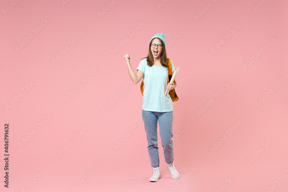 Full length portrait screaming young woman student in t-shirt hat glasses backpack hold notebooks doing winner gesture isolated on pink background. Education in high school university college concept. Full length portrait screaming young woman student in t-shirt hat glasses backpack hold notebooks doing winner gesture isolated on pink background. Education in high school university college concept.