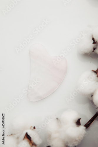Pink Gua Sha massage tool on a white table. Facial skin care at home, anti-aging and lifting therapy. Vertical image. © burdun
