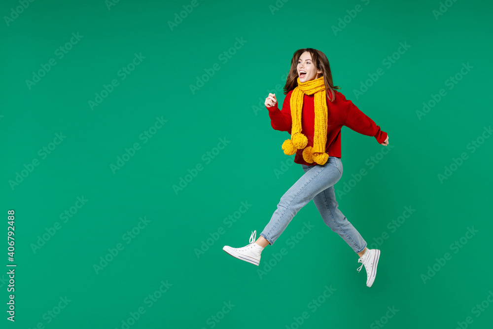 Full length side view of cheerful funny young brunette woman 20s wearing basic casual knitted red sweater yellow scarf jumping like running isolated on bright green color background studio portrait.