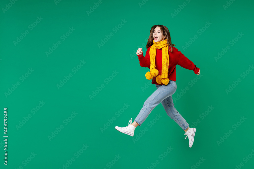 Full length side view of cheerful funny young brunette woman 20s wearing basic casual knitted red sweater yellow scarf jumping like running isolated on bright green color background studio portrait. Full length side view of cheerful funny young brunette woman 20s wearing basic casual knitted red sweater yellow scarf jumping like running isolated on bright green color background studio portrait.