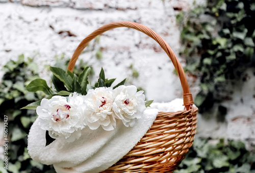 A bouquet of white peonies flowers in a basket outside against a white wall. Spring flowers. Cut peonies in the garden