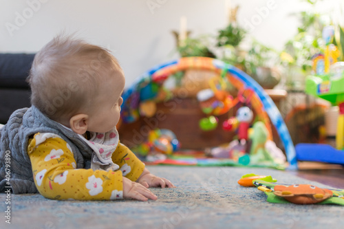6 month old baby doing tummy time on a rug on the floor with colorful toys and plants in the background