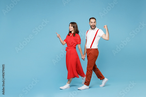 Full length of excited young couple two friends man woman in white red clothes pointing index finger aside doing winner gesture isolated on blue background studio. St. Valentine's Day holiday concept.