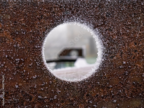 Rusty sheet metal with a hole in the center completely frozen around its circumference, revealing out-of-focus machinery
