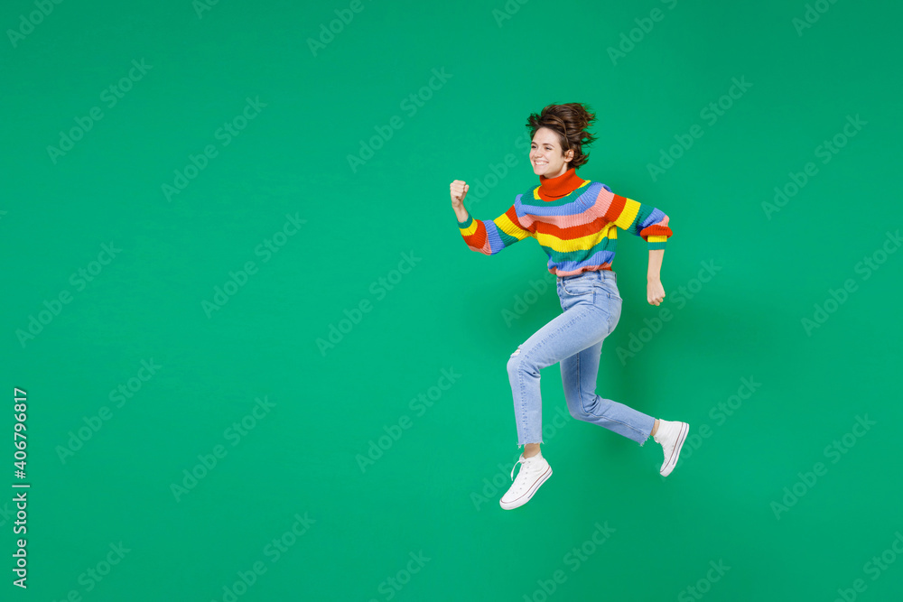 Full length side view of smiling cheerful pretty young brunette woman 20s years old in basic casual colorful sweater jumping like running isolated on bright green color background studio portrait. Full length side view of smiling cheerful pretty young brunette woman 20s years old in basic casual colorful sweater jumping like running isolated on bright green color background studio portrait.