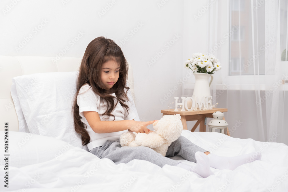 sad little brunette girl sitting with teddy bear on bed at home sad little brunette girl sitting with teddy bear on bed at home
