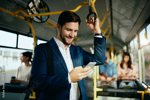 Happy businessman texting on cell phone while commuting to work by bus.