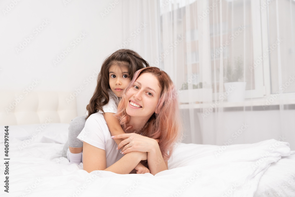 young mother and little active daughter lying on bed at home, hugging, having fun young mother and little active daughter lying on bed at home, hugging, having fun