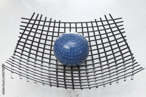 Fototapeta Blue orb sitting on wire mesh looking like earth distorting spacetime to produce