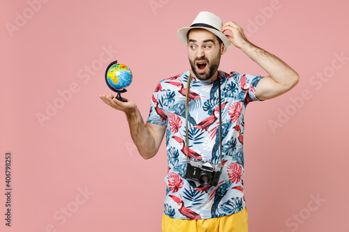 Puzzled young traveler tourist man in summer clothes hat photo camera hold Earth world globe put hand on head isolated on pink background. Passenger traveling on weekend. Air flight journey concept. © ViDi Studio