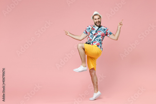 Full length of laughing young traveler tourist man in summer clothes hat point index fingers up dancing isolated on pink background studio. Passenger traveling on weekends. Air flight journey concept.