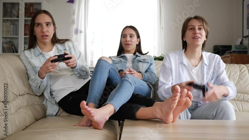 Teenager girls at home triplet sisters have fun play console games sitting on couch at home stay isolated under quarantine
