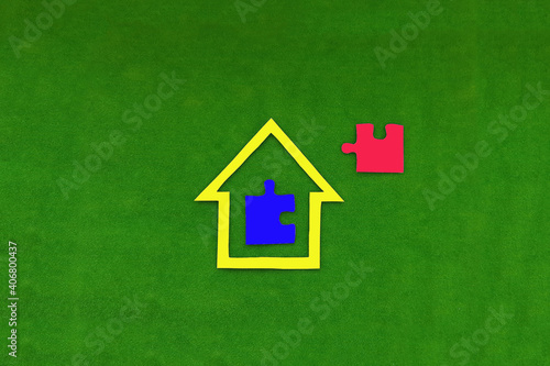 The house is yellow, two pieces of puzzles are red and blue on a green background. Shared ownership, real estate market.