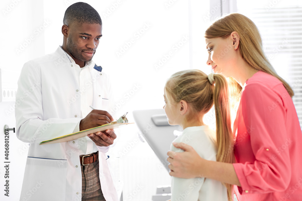 black male doctor talking to child and his mother during health checkup at the clinic, mom and girl get consultation by professional pediatrician or general practitioner during visit to the hospital