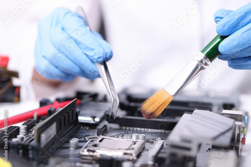 Gloved handyman with brush and tweezers repairs motherboard