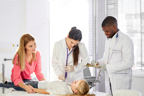 team of doctors working together while treating kid girl patient lying on hospital bed, african man and caucasian woman consulting girl and holding medical check-up © alfa27