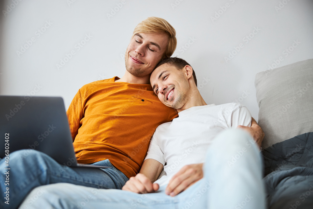Happy homosexual couple cuddling and using laptop at home