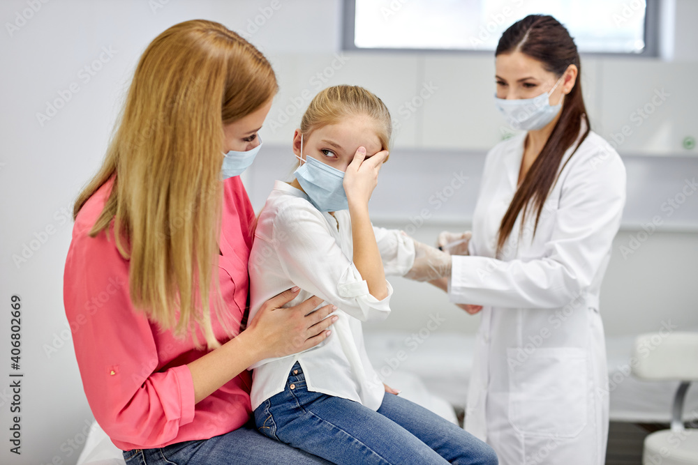 female doctor taking blood sample test of a little girl in the clinic, scared girl sits with mother, woman technician making blood tests on child in the laboratory of blood extractions female doctor taking blood sample test of a little girl in the clinic, scared girl sits with mother, woman technician making blood tests on child in the laboratory of blood extractions