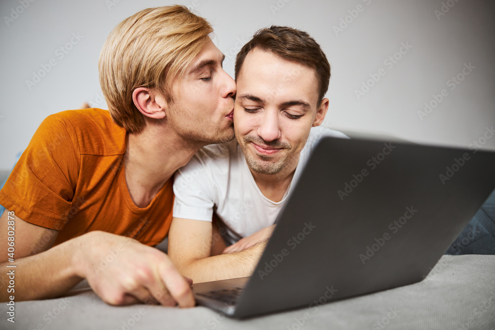 Happy gay couple using laptop and sharing tender kiss Happy gay couple using laptop and sharing tender kiss