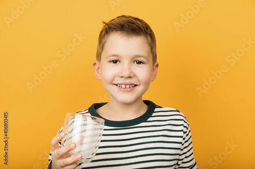 Happy little boy with milk moustache holding empty glass isolated on yellow background. Milk benefits, healthy food concept.